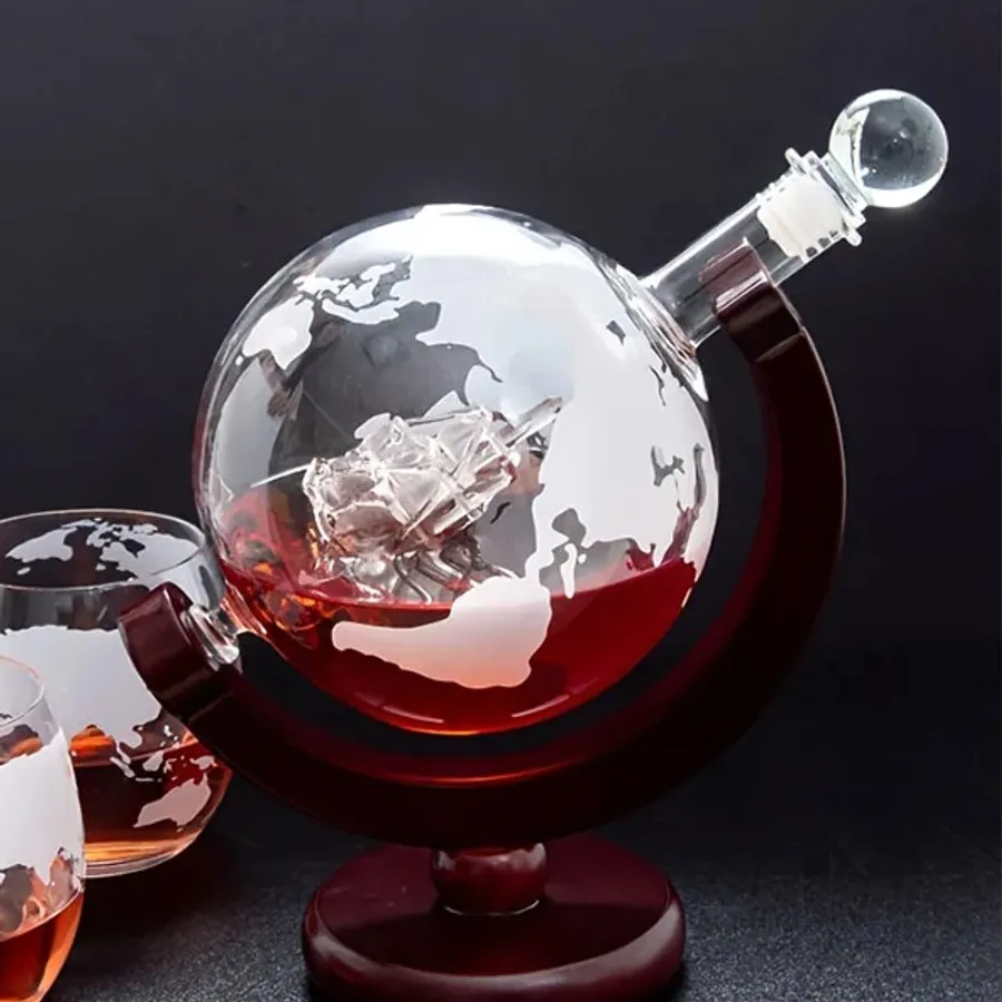 An etched globe whisky decanter and two matching tumblers on a dark surface