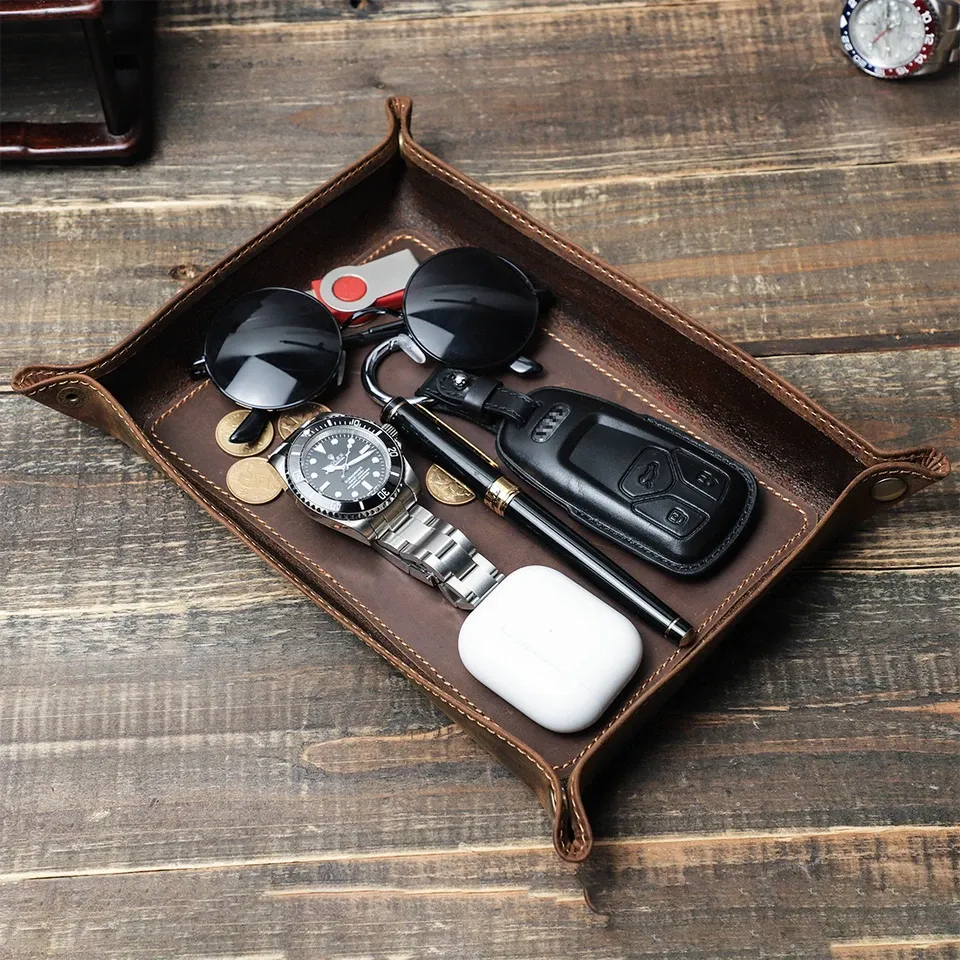 A folded cowhide valet tray holding keys, a watch and sunglasses