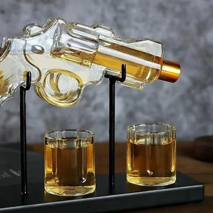 A revolver-shaped glass decanter on a stand with two filled shot glasses